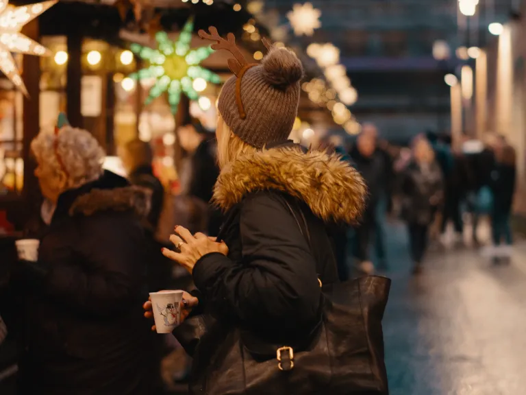 A woman standing in line surrounded by people and Christmas lights.