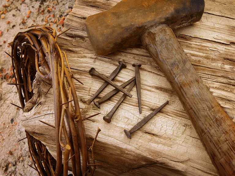 Photo illustration of a crown of thorns, old nails, hammer and wood beam.