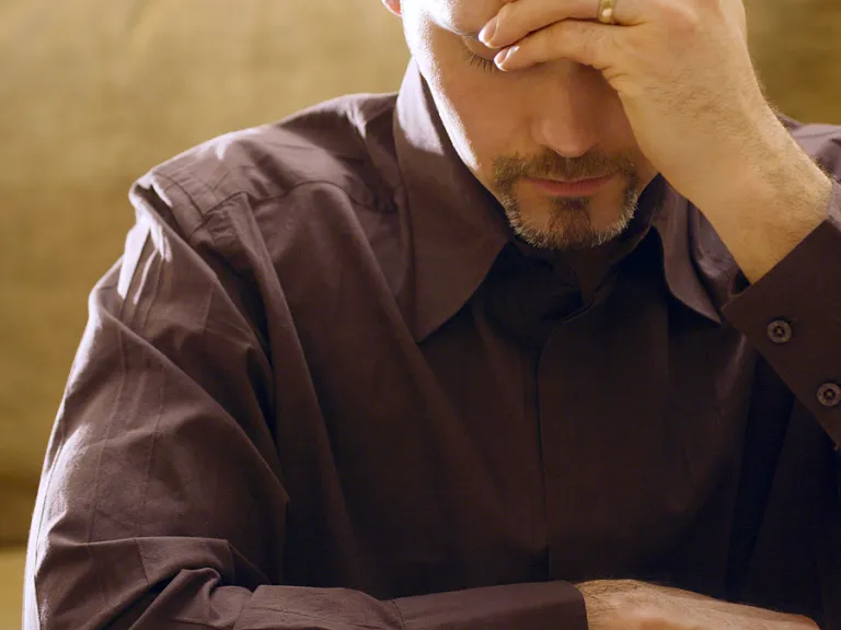 A man with his hand holding his head while looking down at a Bible.
