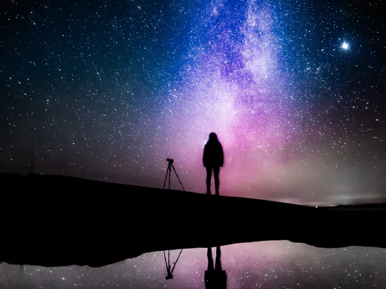 Silhouette of a person with a telescope against a gorgeous starry sky