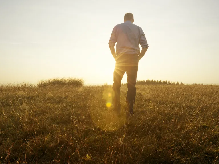 Photo of a man walking in a field toward the sun at golden hour.