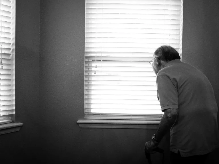 An elderly man looking out a window.