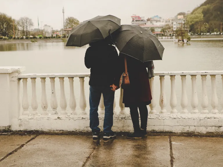 A couple standing on a bridge with umbrellas