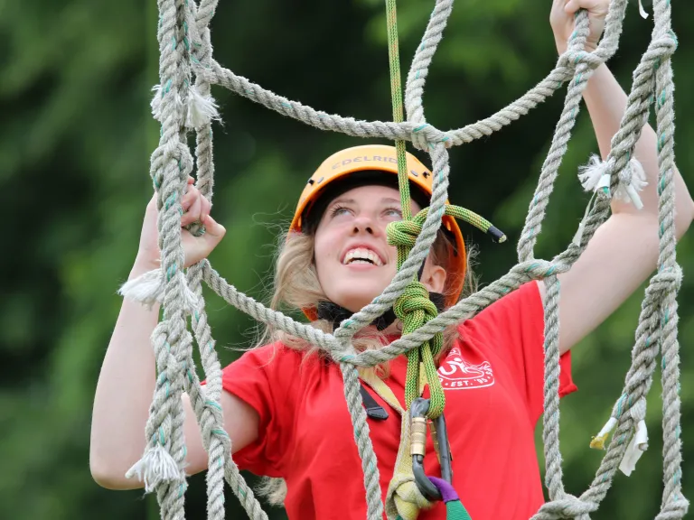 a teenage girl climbing a rope ladder with a smile