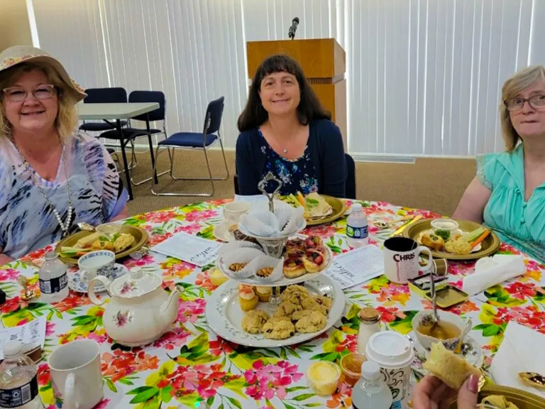 three ladies seated at a table enjoying tea and desserts