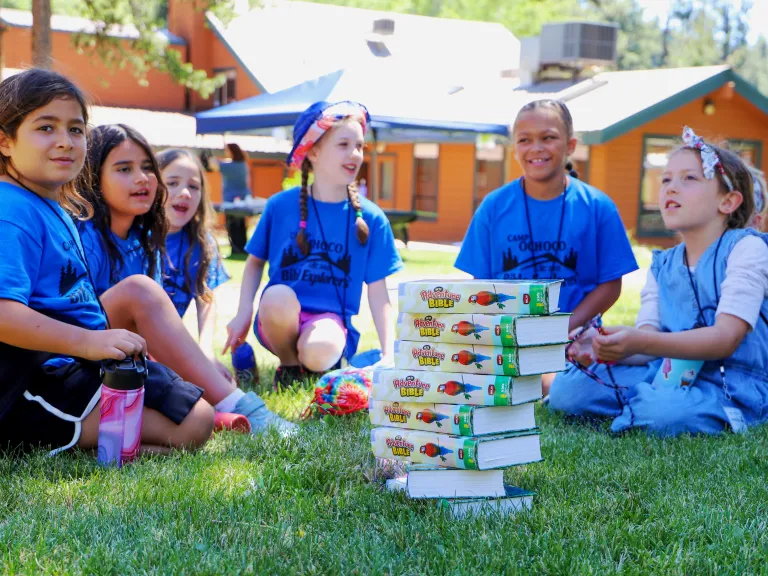 a group of girls sitting around a stack of Bibles