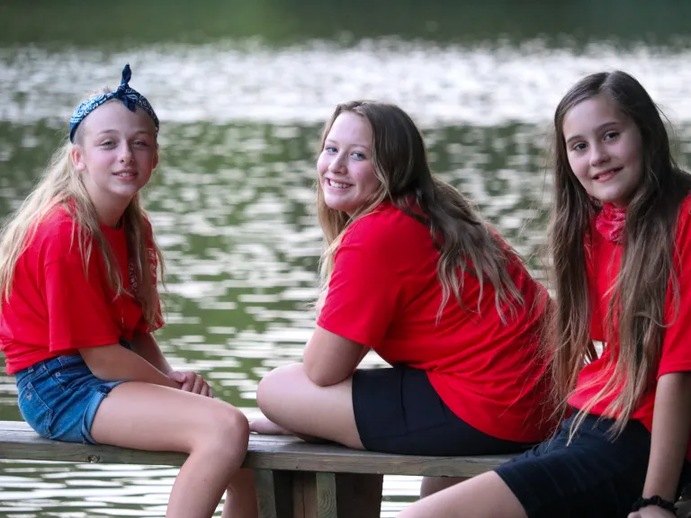 three girls sitting on a bench by the lake