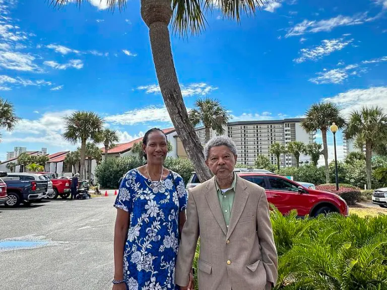 a couple standing outdoors in front of a palm tree