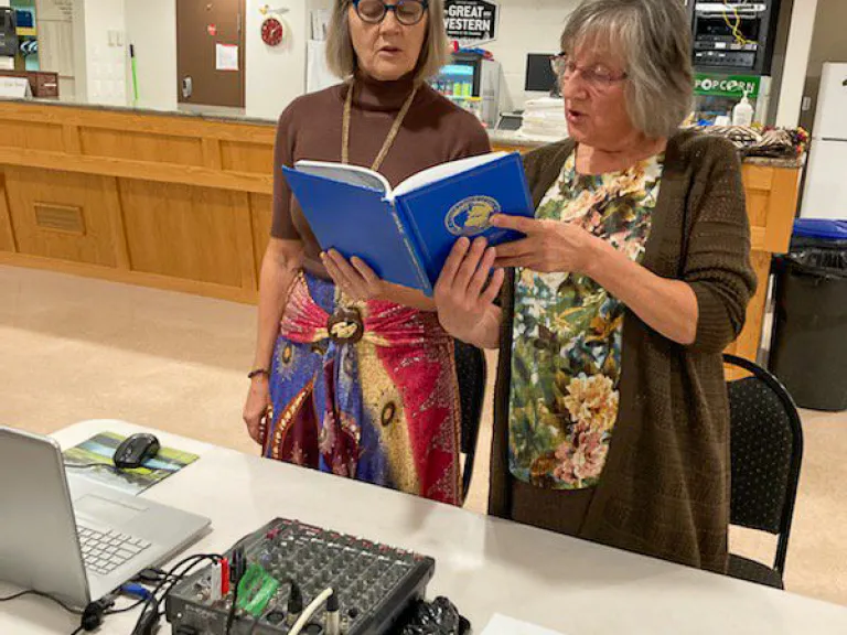 two women singing hymns while standing at the sound table