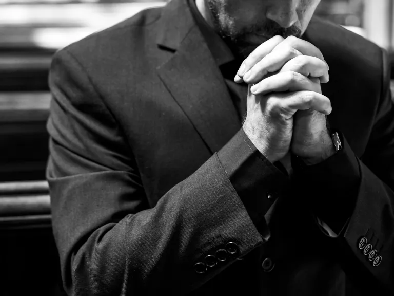 a man in a suit with hands folded in prayer