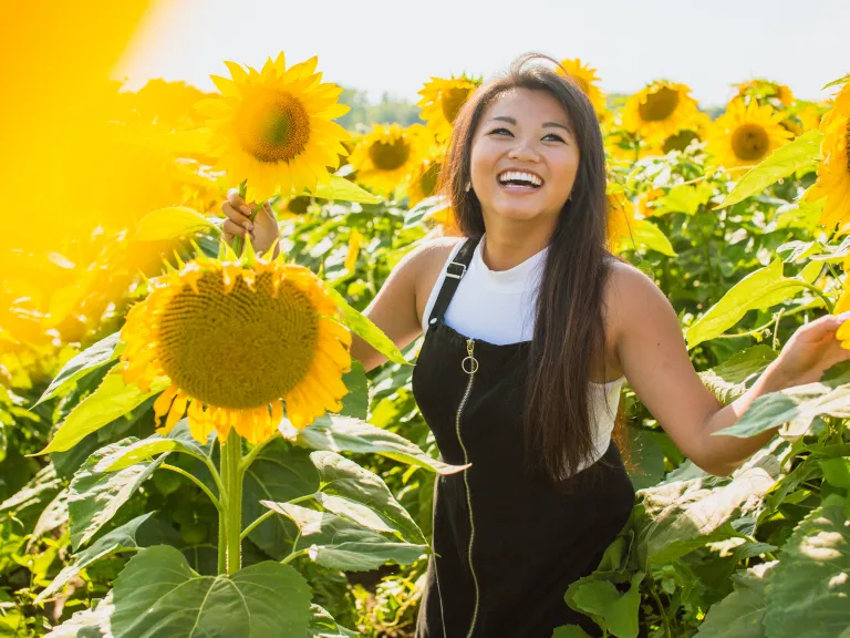 a smiling woman standing in a field of sunflowers