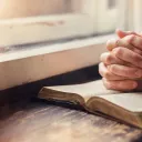 A woman reading a Bible by a window.