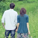 A young married couple holding hands standing in a grass field.